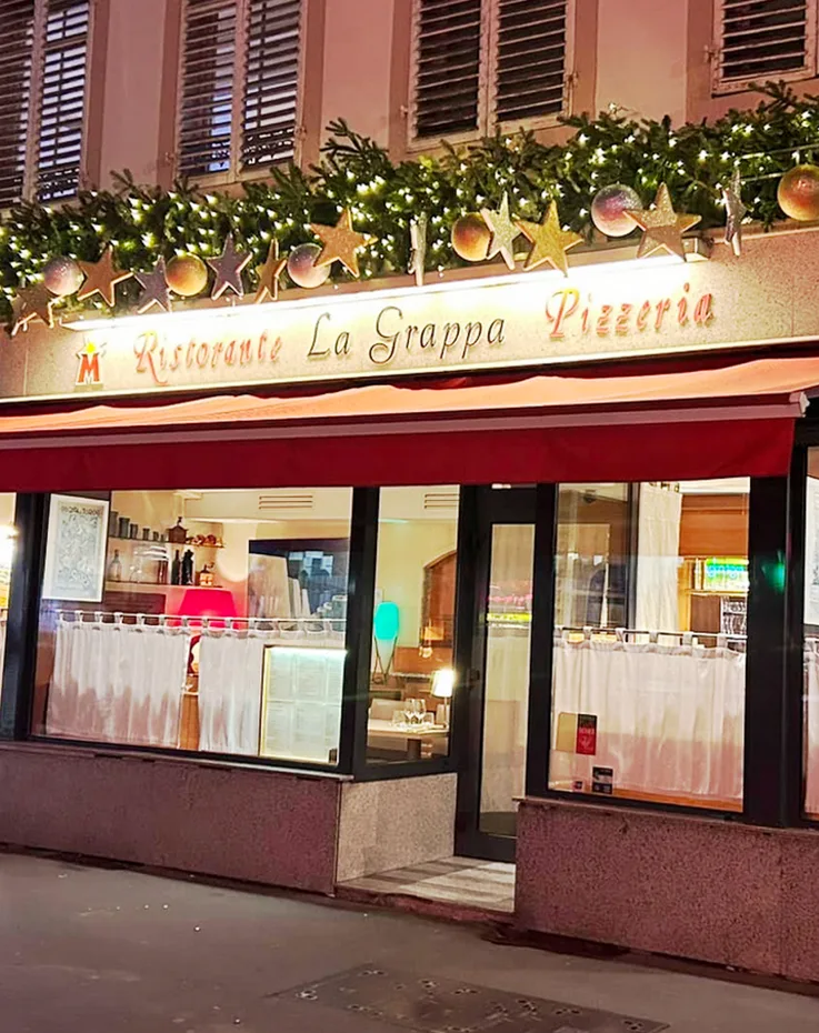 La devanture de La Grappa le soir : guirlande, enseigne Ristorante La Grappa Pizzeria et auvent rouge